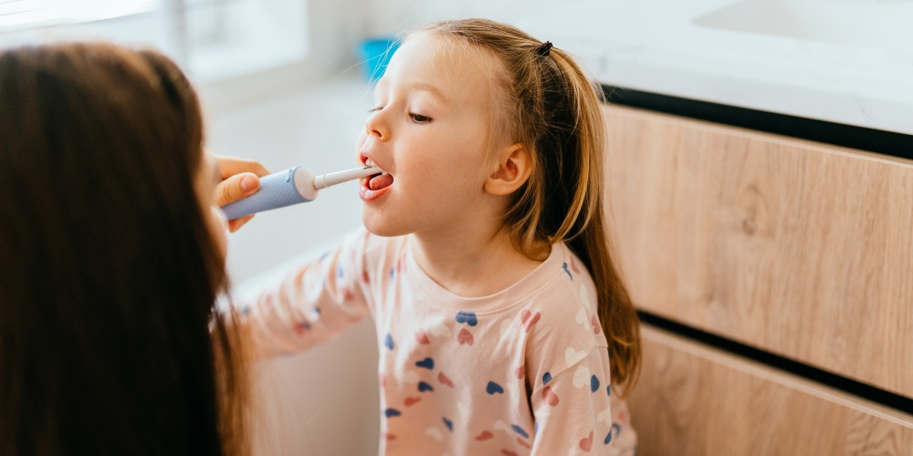mama uczy córkę myć zęby szczoteczką elektryczną