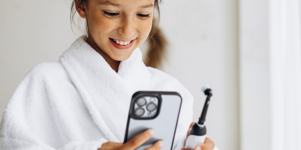 dziewczynka myje zęby szczoteczką elektryczną i korzysta z aplikacji mobilnej