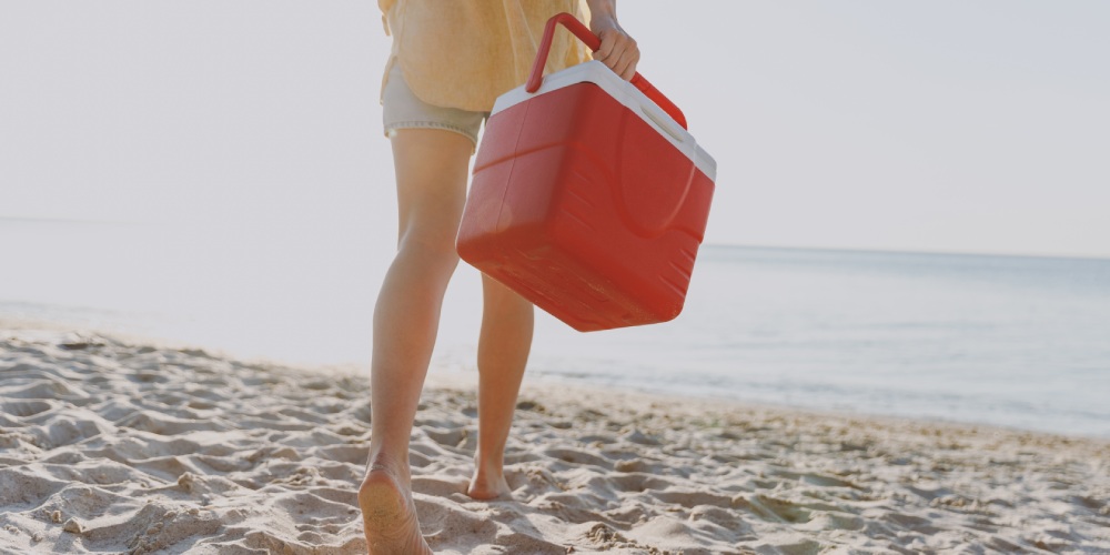 kobieta idzie po plaży z lodówką turystyczną