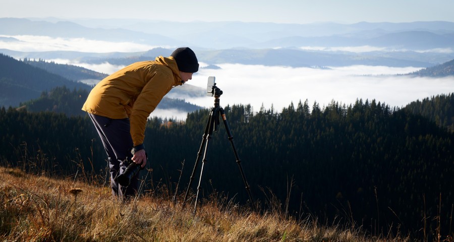 fotograf stojący w górach ze smartfonem na statywie